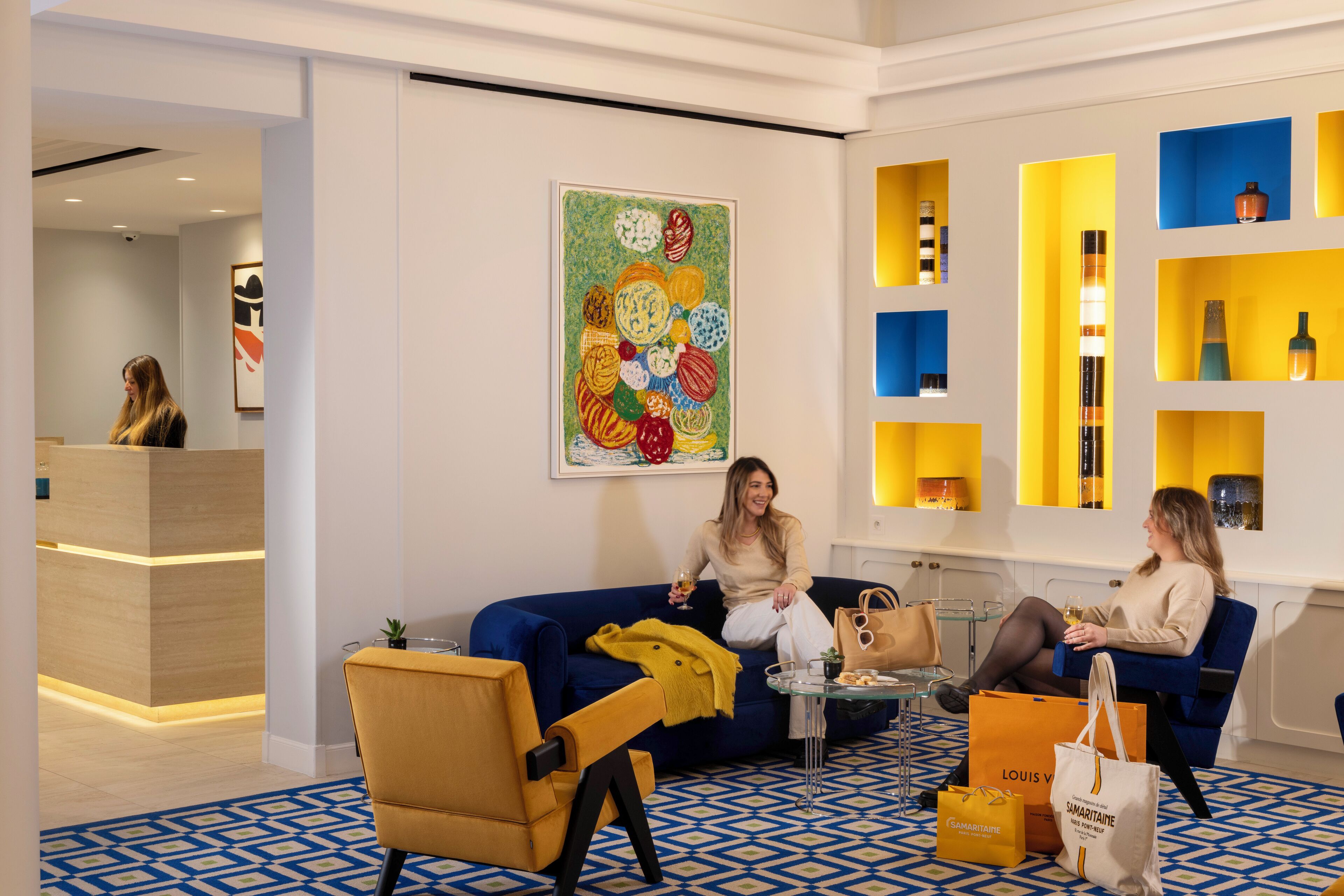 Um lobby moderno com esquema de cores azul e amarelo, apresentando um balcão de recepção, um sofá azul e um piso estampado.