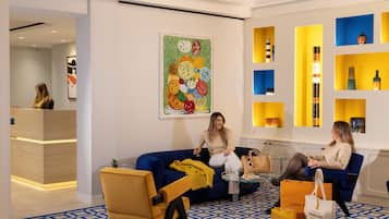 Um lobby moderno com esquema de cores azul e amarelo, apresentando um balcão de recepção, um sofá azul e um piso estampado.