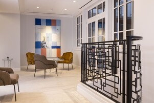 A modern interior with a geometric black partition, a white-framed window, and a seating area with two chairs and a table.
