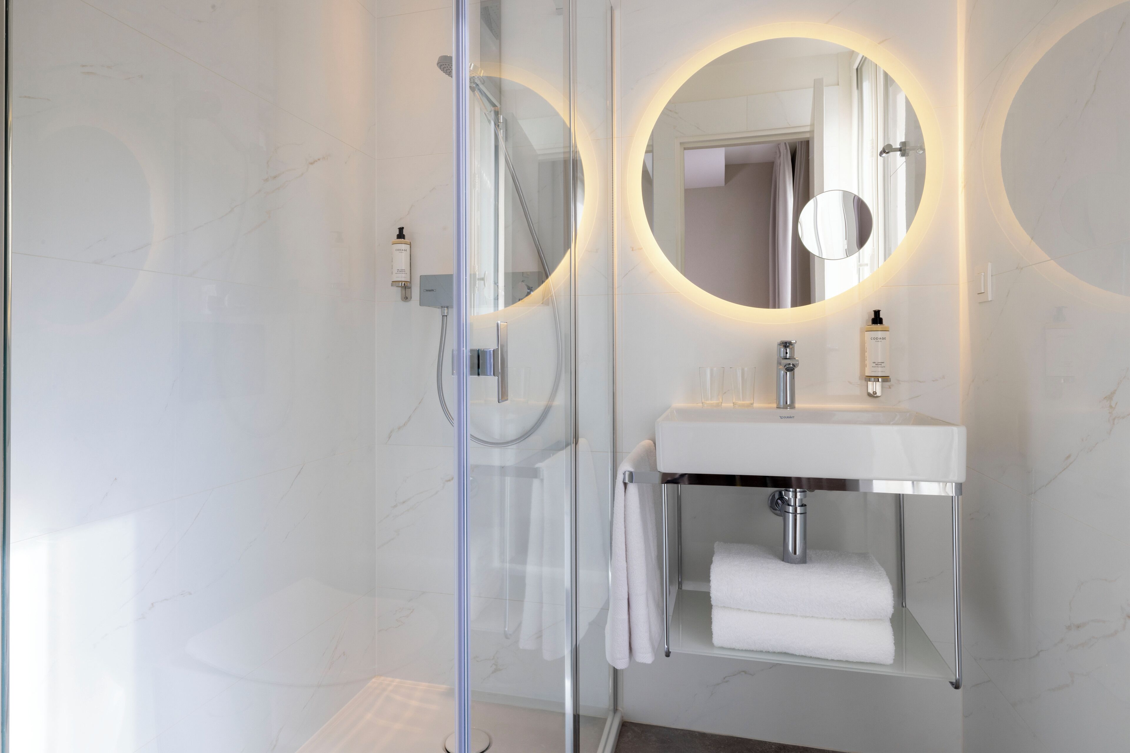 Un baño moderno con cabina de ducha de vidrio, lavamanos blanco con espejo y un perchero para toallas.