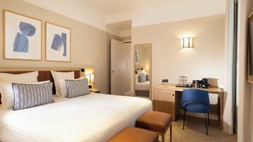 Quarto de hotel com uma cama grande, uma escrivaninha, uma cadeira e um espelho.