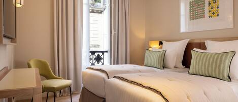 A hotel room with two beds, a desk, a chair, and a balcony with a railing.