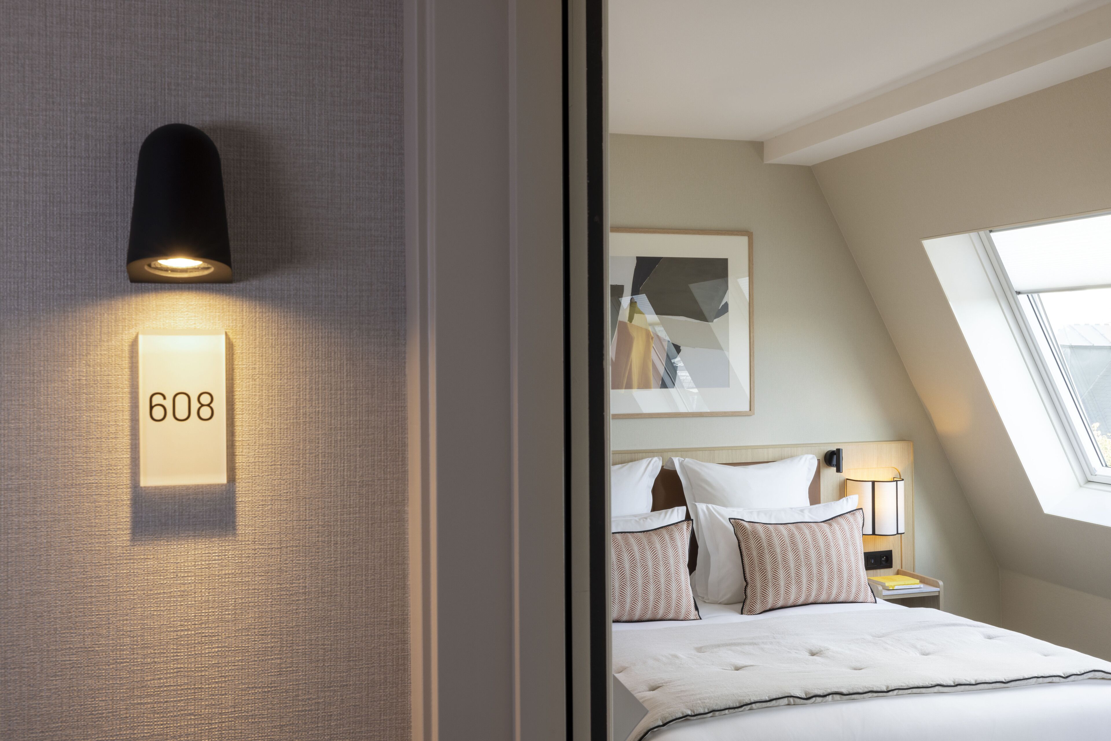 Habitación de hotel con cama, luz empotrada, letrero con número y tragaluz.