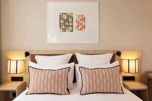 A hotel room with a neatly made bed, two bedside lamps, and a framed artwork above the bed.