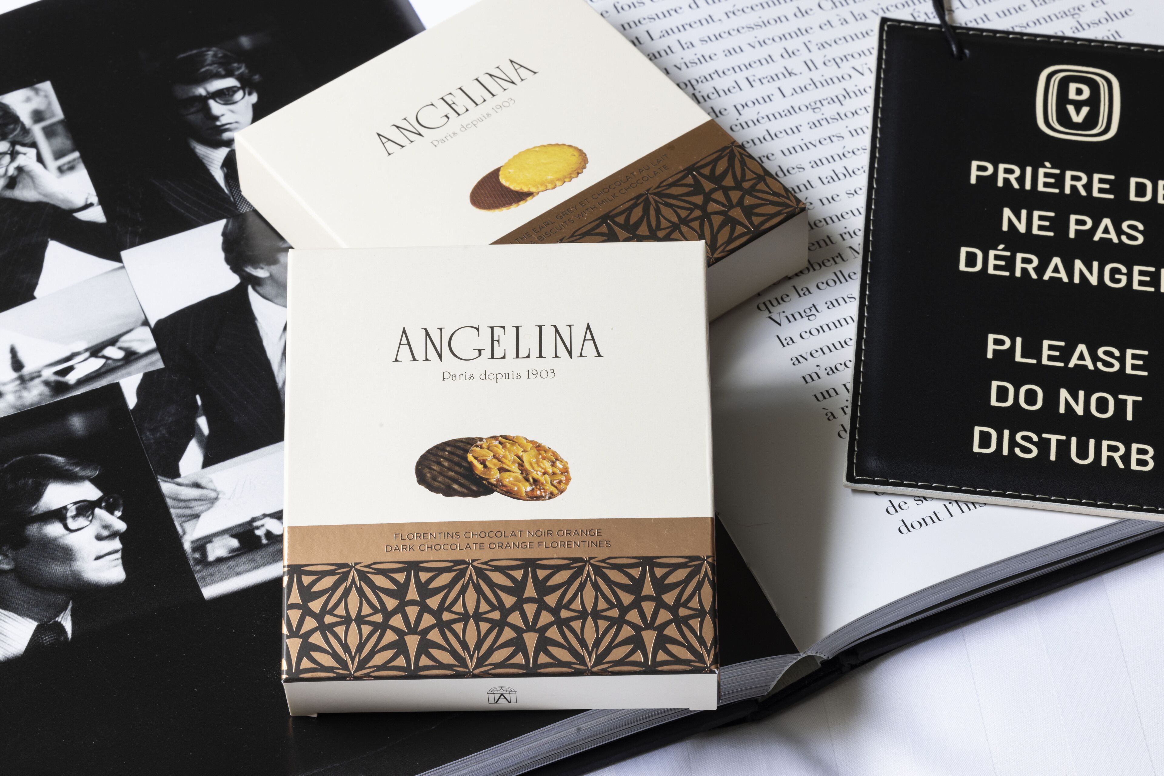 Dos cajas de chocolate negro Angelina sabor naranja con almendras, un libro y un cartel con texto en francés.
