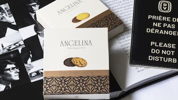 Dos cajas de chocolate negro Angelina sabor naranja con almendras, un libro y un cartel con texto en francés.