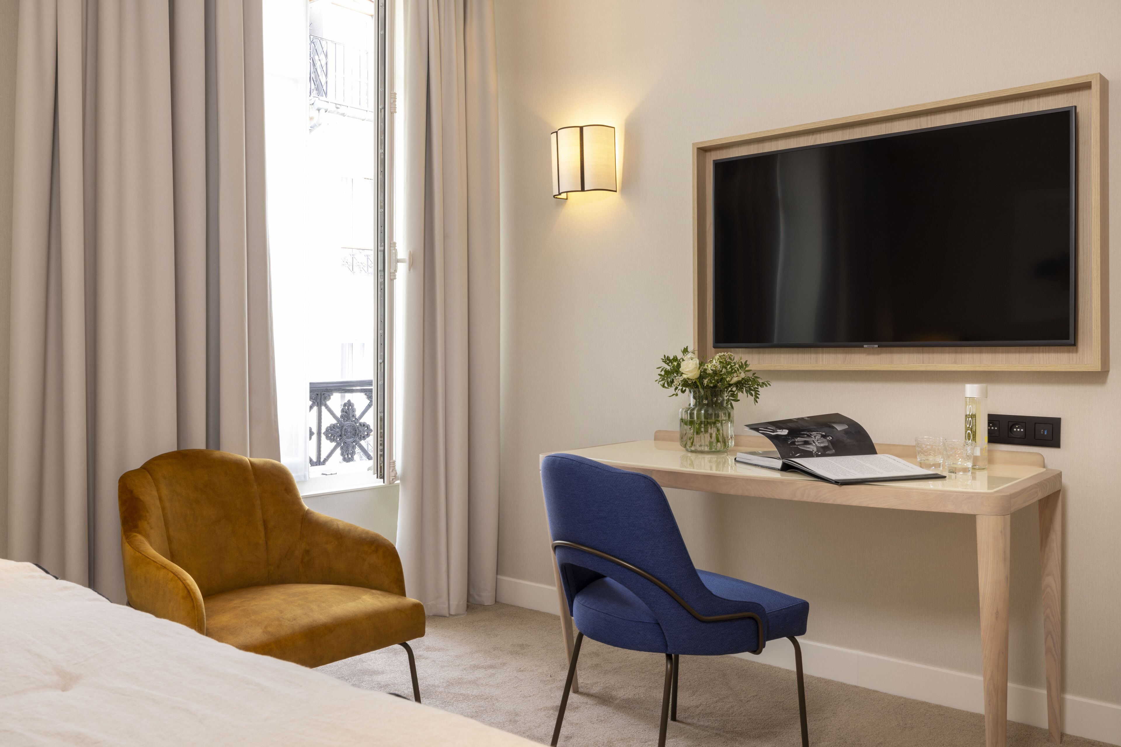 A hotel room with a bed, a desk with a chair, a TV, and a window with curtains.