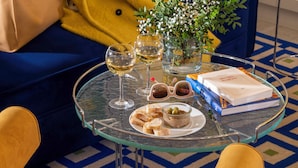 Una mesa de vidrio con copas de vino, un plato de comida, un libro y un florero con flores.