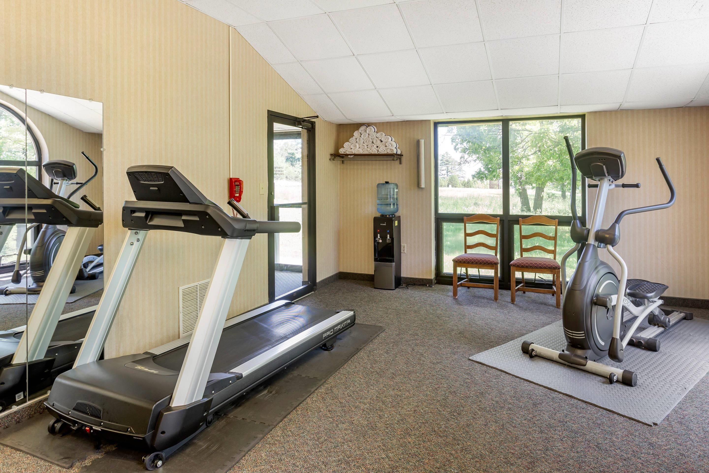 A gym with treadmills, a water dispenser, and a view of trees through large windows.