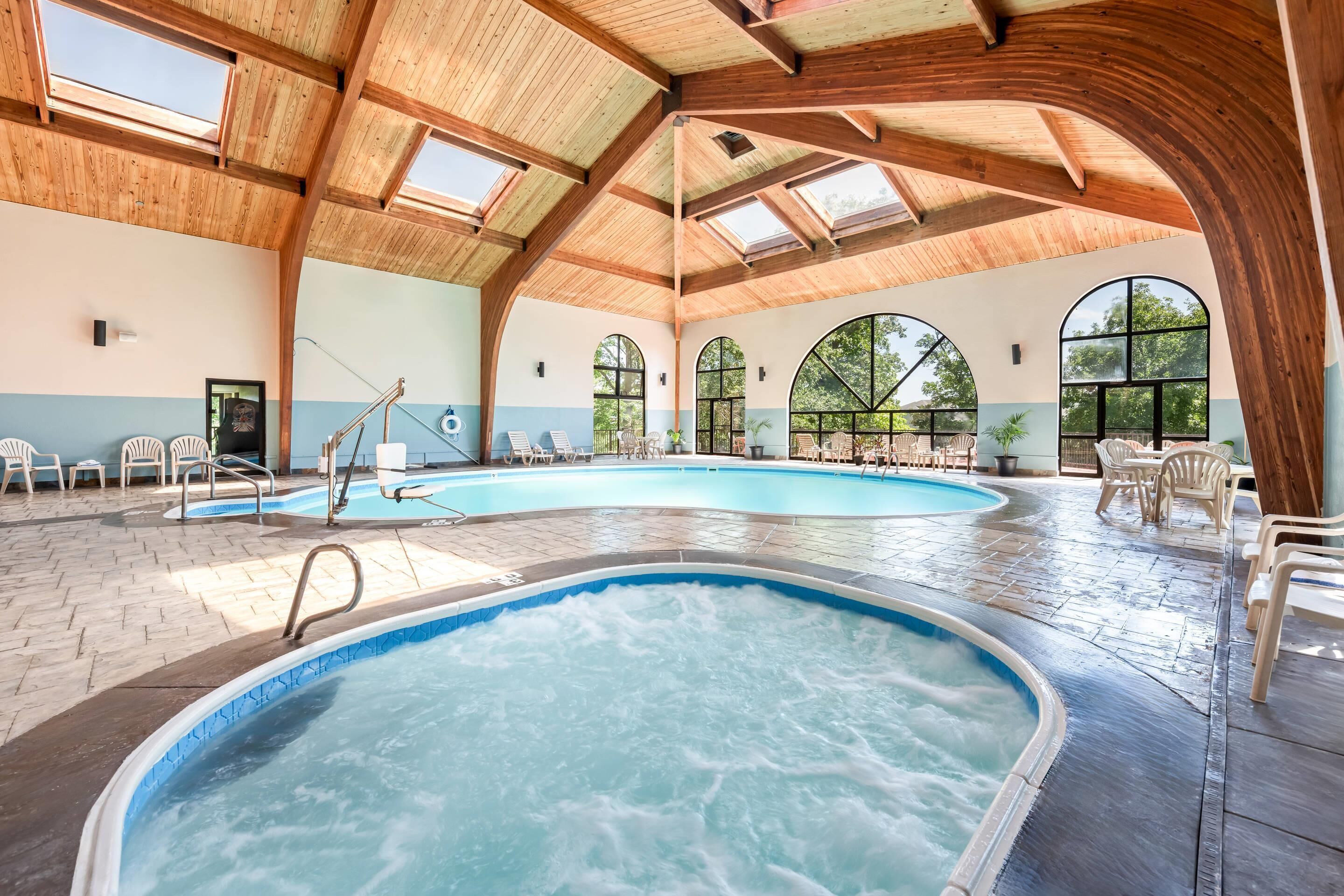 An indoor swimming pool with multiple lanes, wooden ceiling beams, and large arched windows.