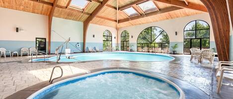 An indoor swimming pool with multiple lanes, wooden ceiling beams, and large arched windows.