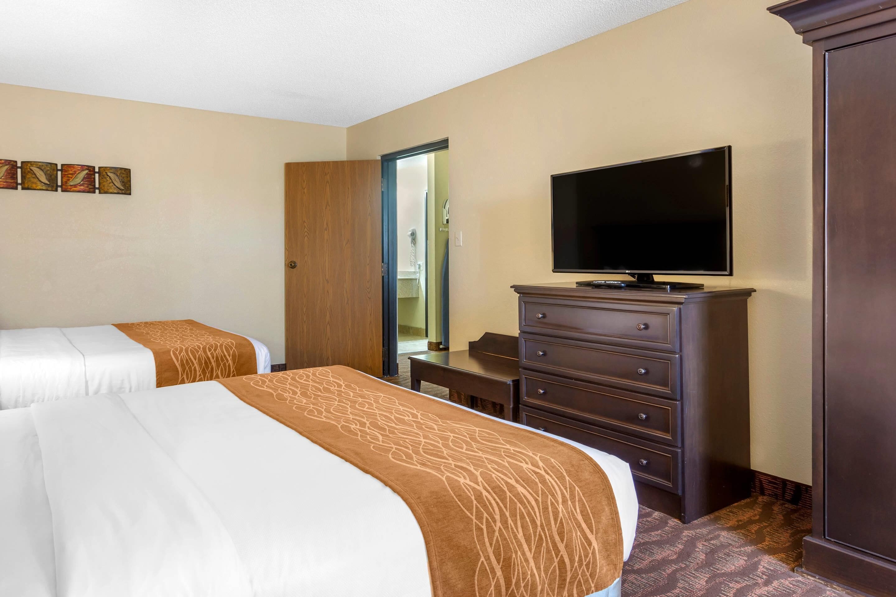 A hotel room with two beds, a television, a dresser, and a door leading to a bathroom.