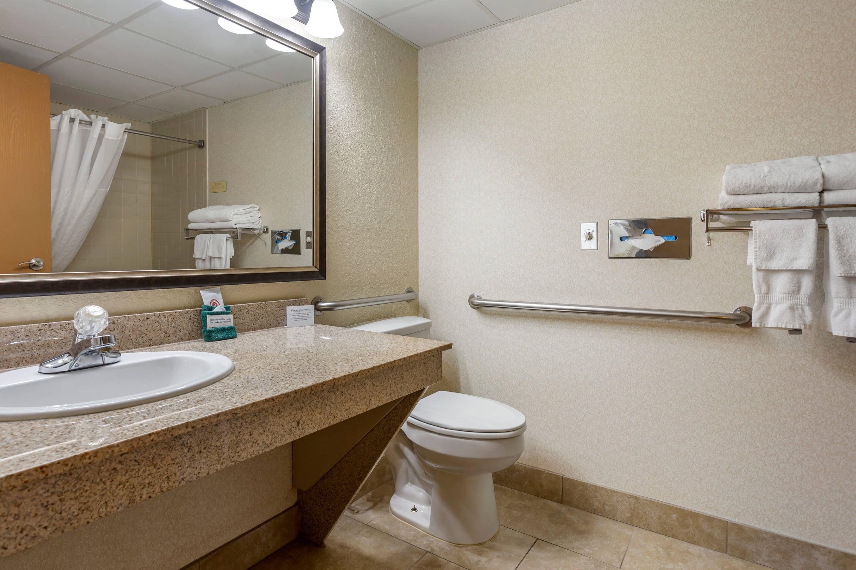 A bathroom with a sink, mirror, toilet, towel rack, and hand dryer.