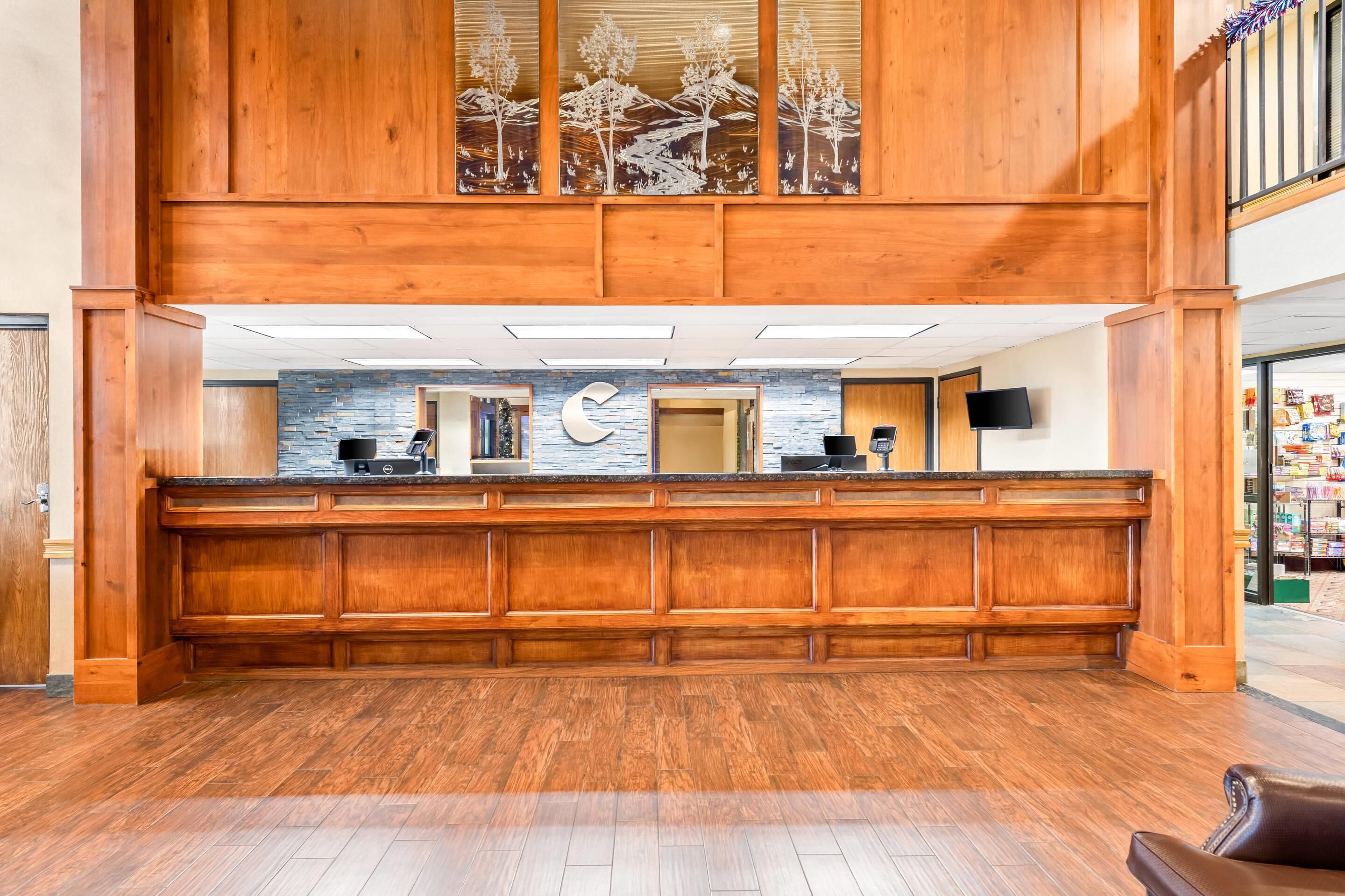 A reception desk with a wooden finish, a stone wall with a clock, and a staircase in the background.