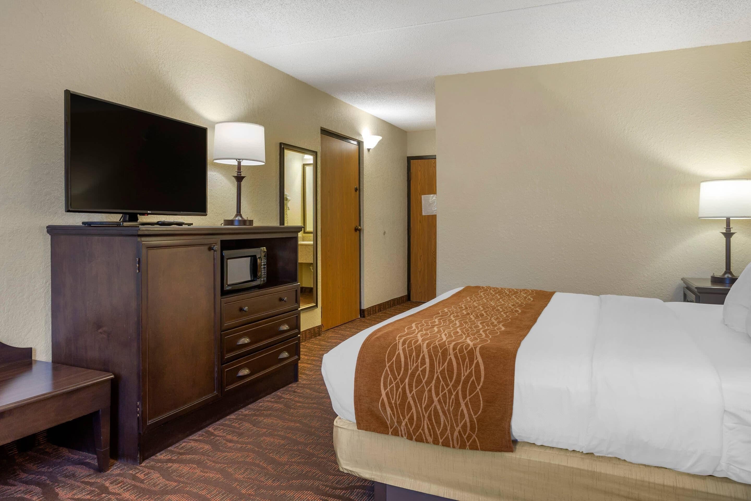 A hotel room with a bed, a TV, a desk, a dresser, and a door.