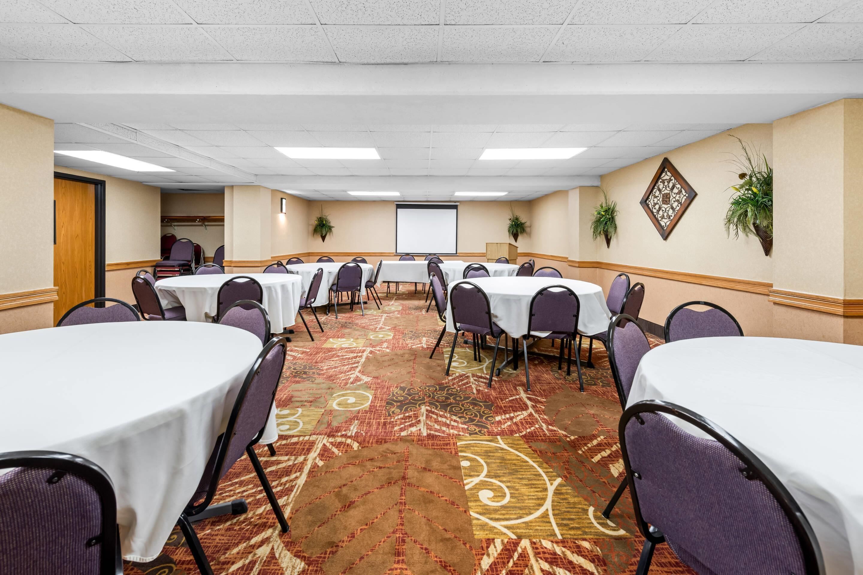 A conference room with multiple round tables, chairs, and a projector screen.
