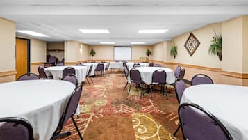 A conference room with multiple round tables, chairs, and a projector screen.