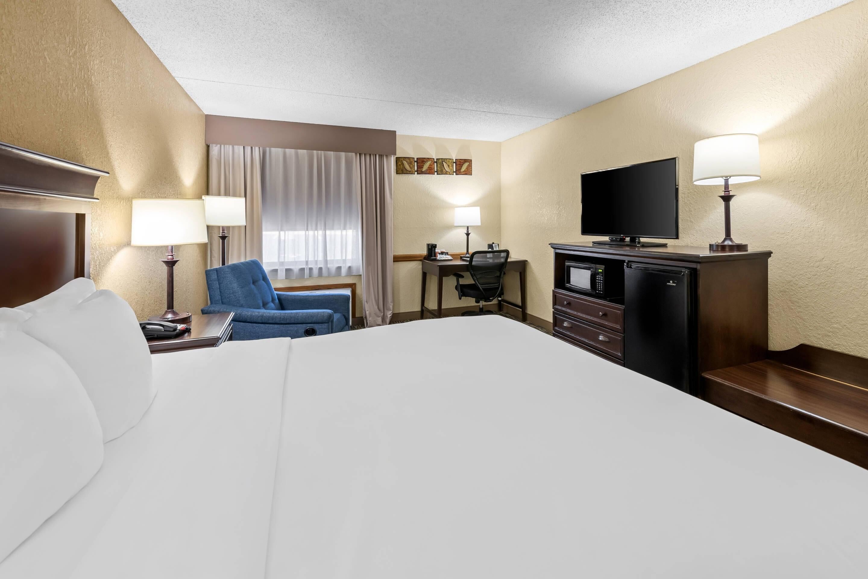 A hotel room with a large bed, a desk with a chair, a television, and a minibar.