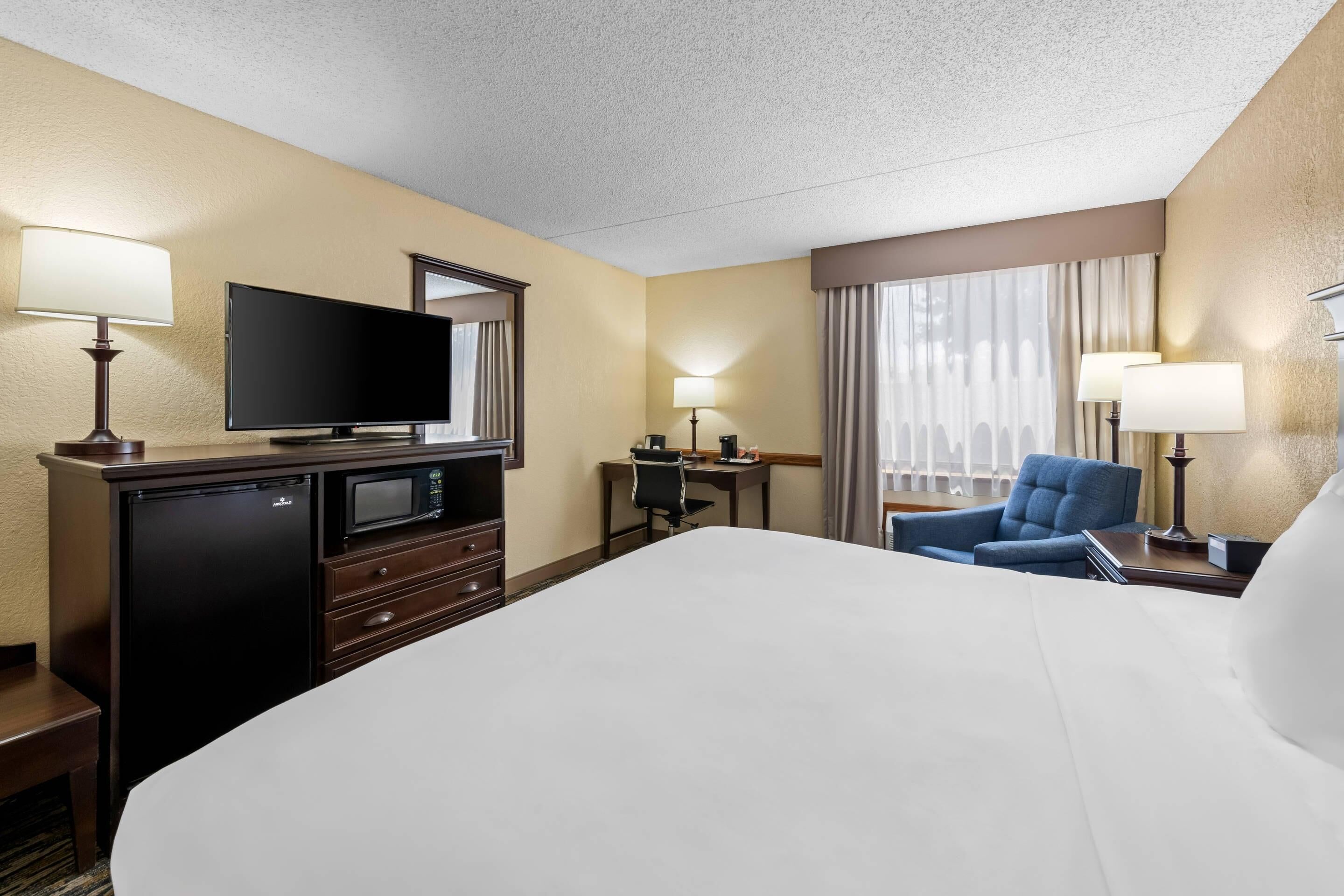 A hotel room with a bed, a television, a desk with a chair, and a window with curtains.