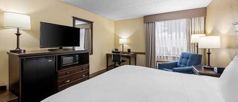 A hotel room with a bed, a television, a desk with a chair, and a window with curtains.