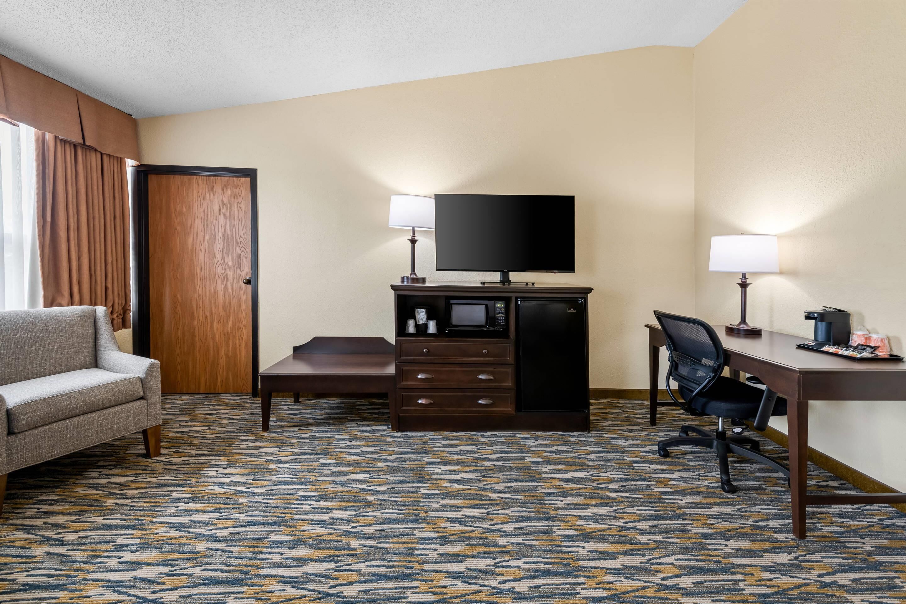 Habitación de hotel con sofá, escritorio, silla, televisión, microondas y minibar.
