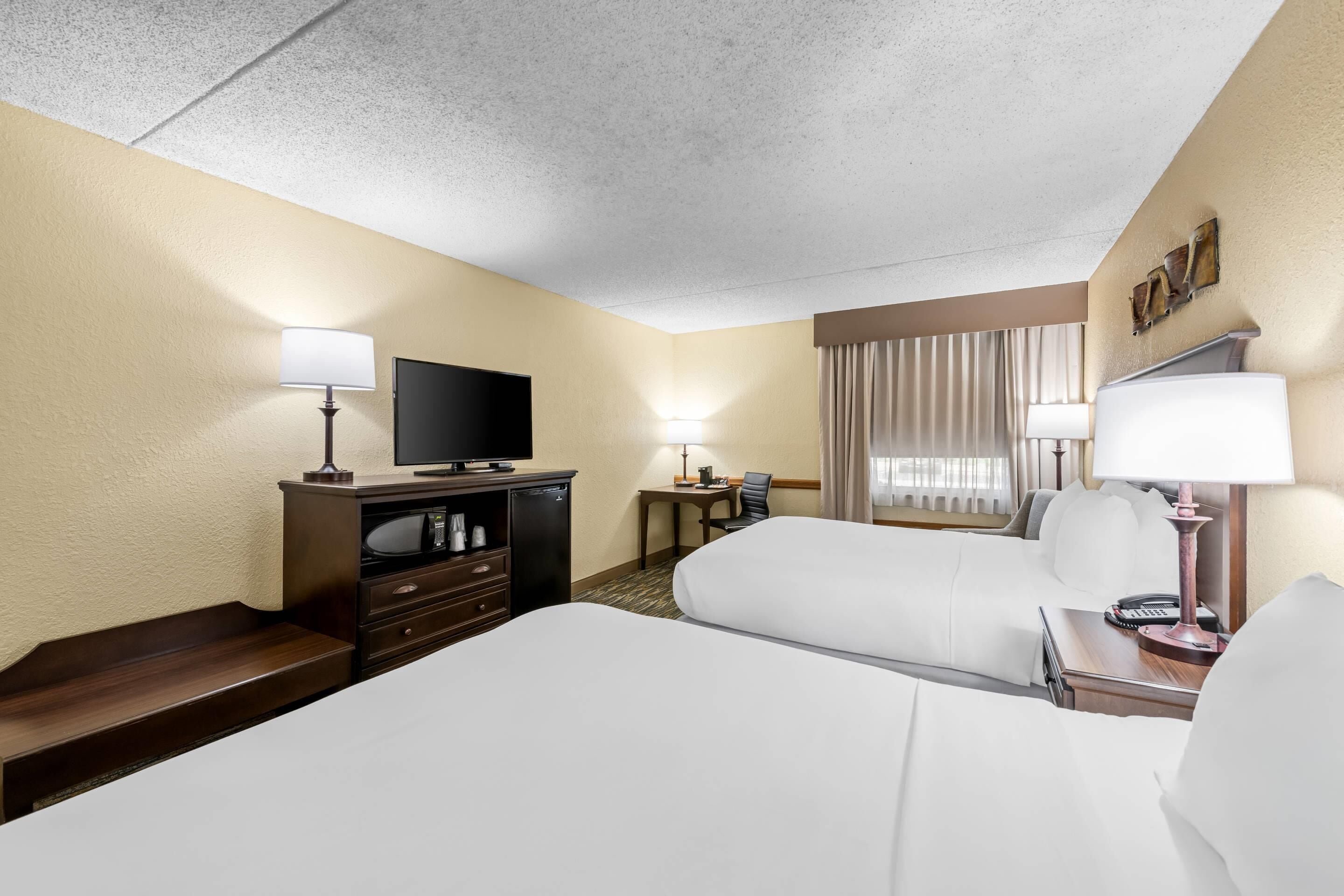 A hotel room with a bed, a TV, a desk, a chair, and a lamp.