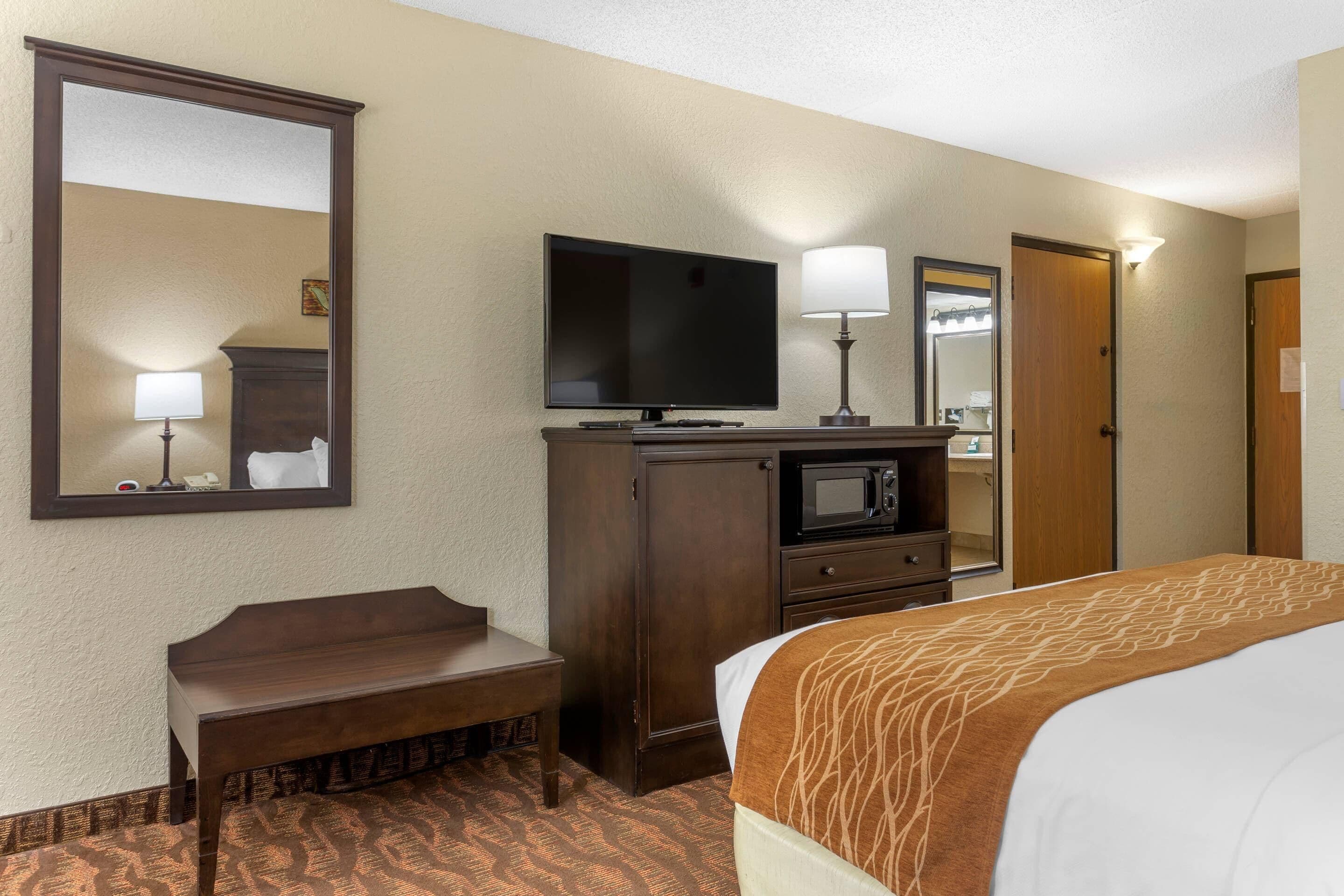 A hotel room with a bed, a desk, a television, a microwave, and a mirror.