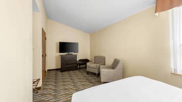 A hotel room with a bed, a television, a desk, and two chairs.