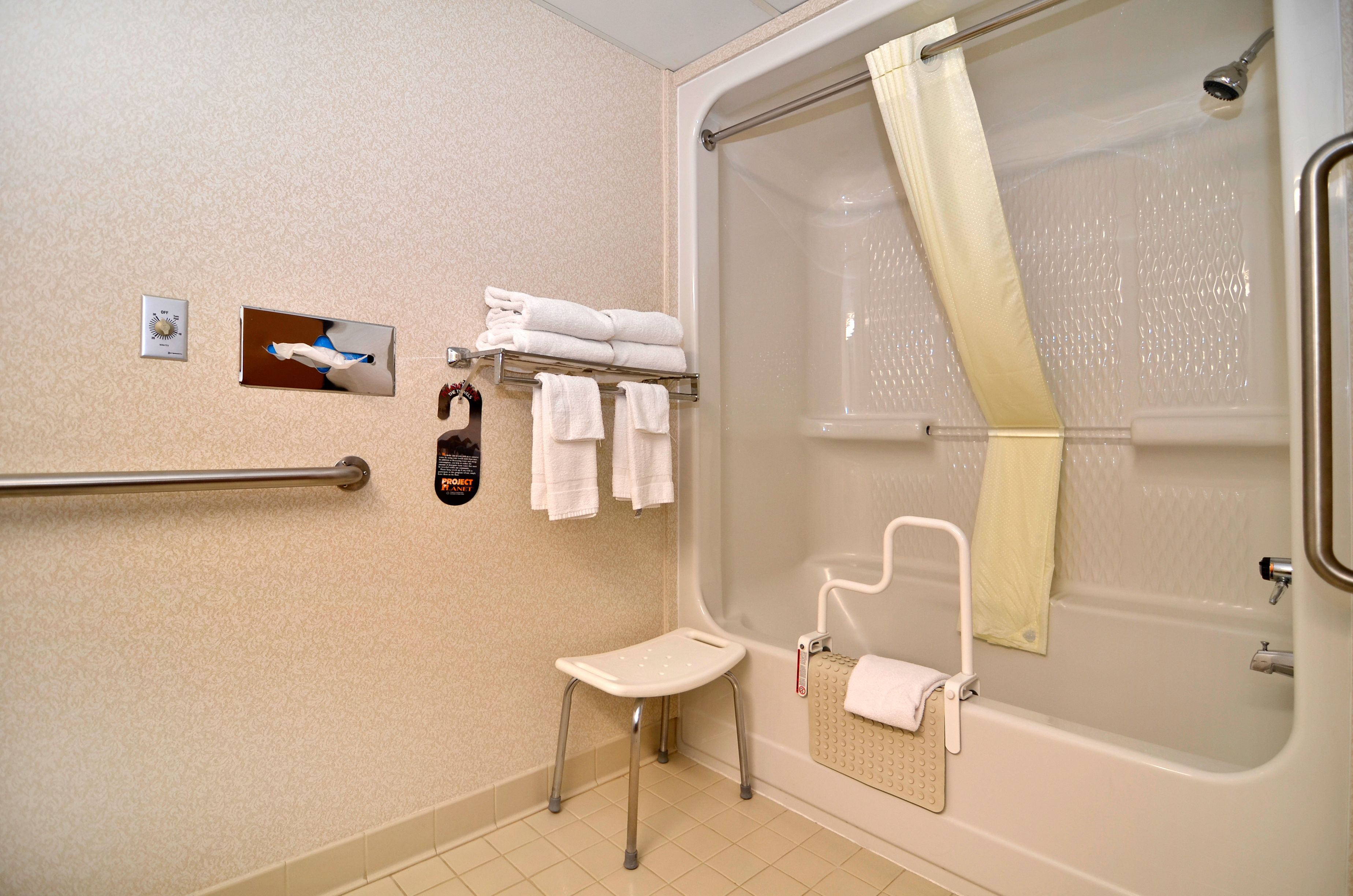 A bathroom with a walk-in shower, a grab bar, a small stool, and a towel rack with folded towels.