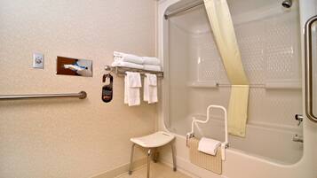 A bathroom with a walk-in shower, a grab bar, a small stool, and a towel rack with folded towels.