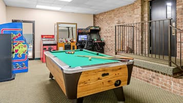 A pool table in a room with a brick wall, a door, and arcade games.
