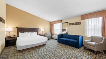 Habitación de hotel con una cama grande, un sofá azul, una silla y un escritorio con lámpara.