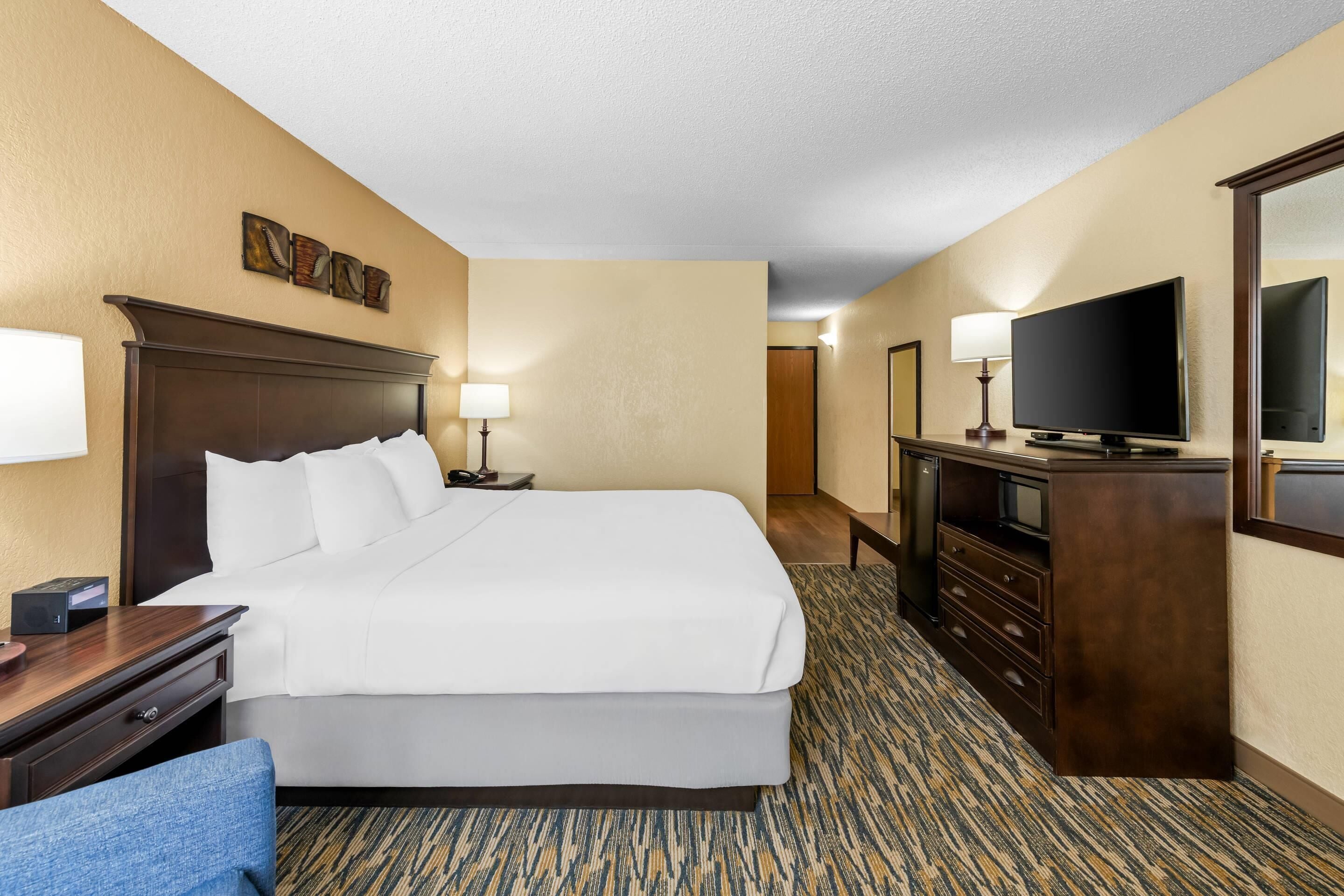 Una habitación de hotel con una cama grande, mesitas de noche, televisión y un escritorio con silla.