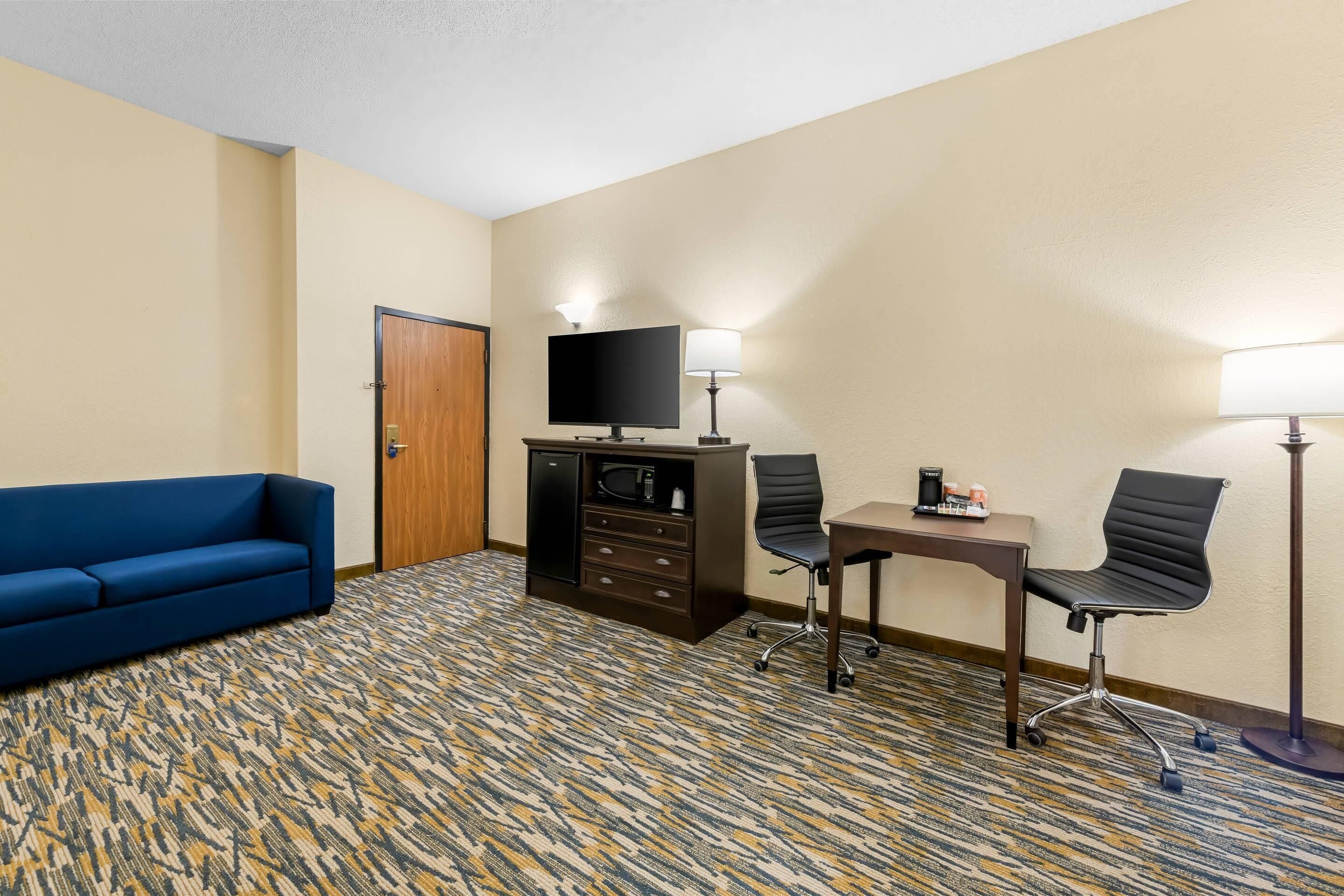 Une chambre d’hôtel avec un canapé bleu, un bureau avec deux chaises, une télévision et un minibar.