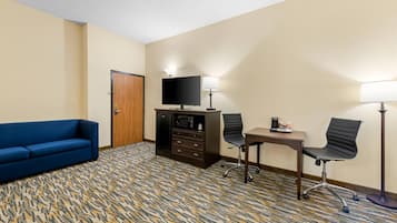 Habitación de hotel con un sofá azul, un escritorio con dos sillas, un televisor y un minibar.
