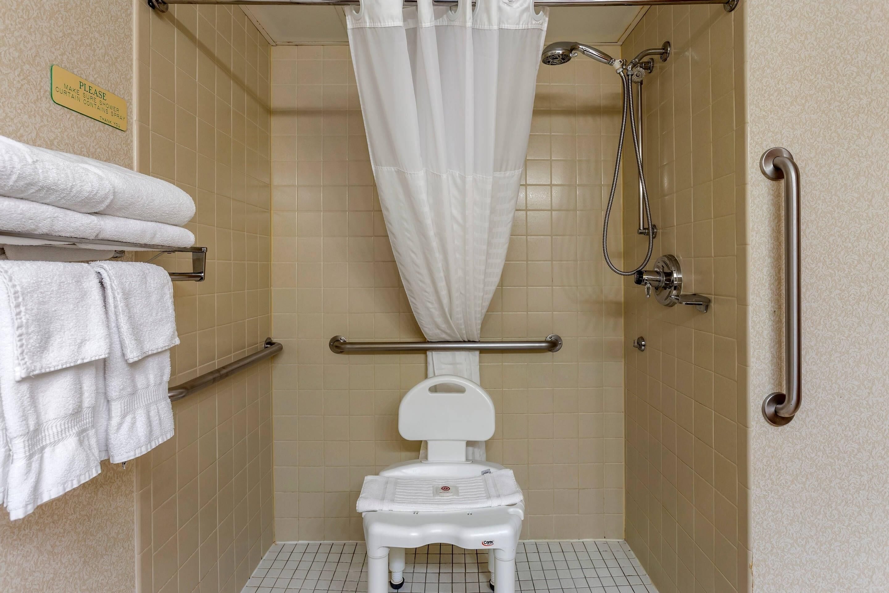 A wheelchair-accessible shower stall with a white shower curtain, a grab bar, and a white toilet.