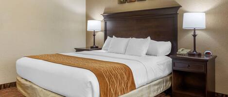 A hotel room with a large bed, two bedside tables with lamps, a nightstand with a phone, and a wall clock.