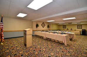 A conference room with a patterned carpet, a podium, tables with chairs, and an American flag.