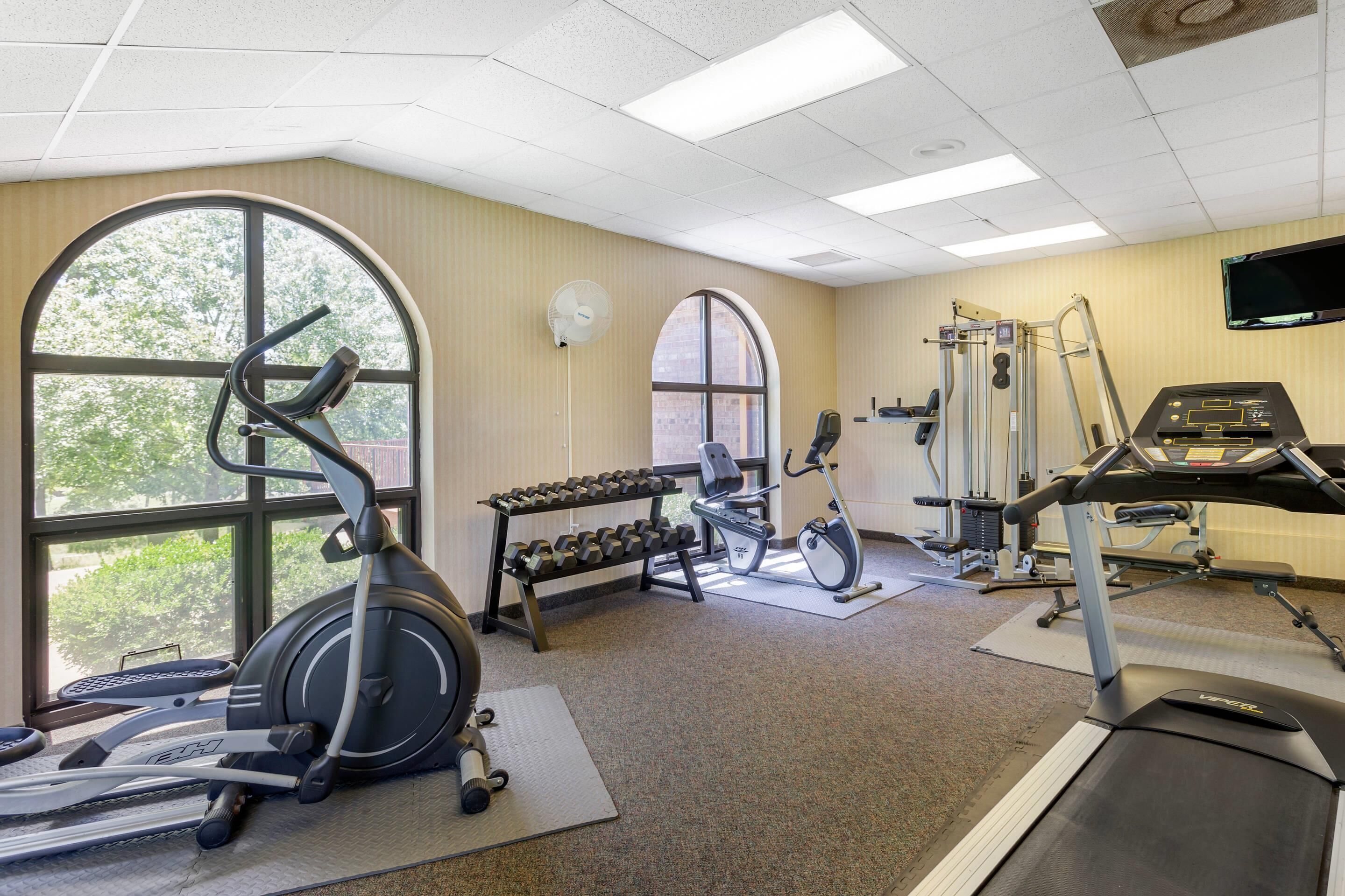A gym with cardio equipment, dumbbells, and a TV screen.