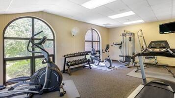 A gym with cardio equipment, dumbbells, and a TV screen.