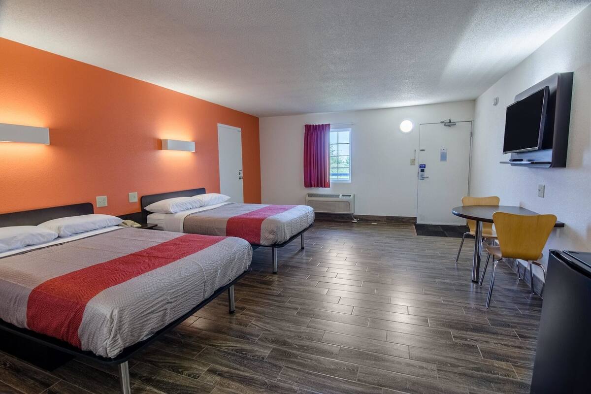 A hotel room with two beds, a desk, a chair, a TV, and a window with curtains.