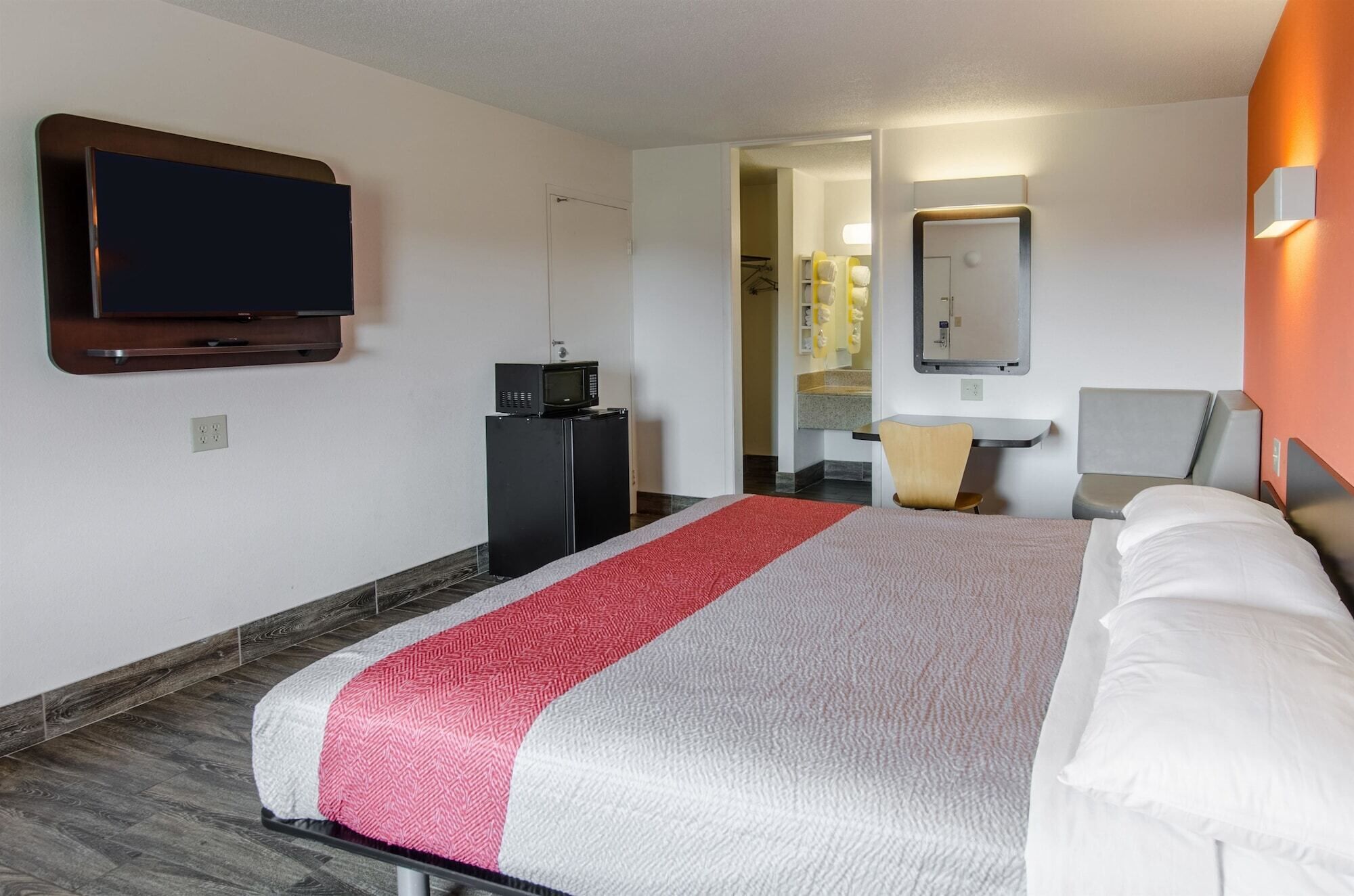 A hotel room with a bed, a TV, a microwave, a desk, and a bathroom visible through an open door.