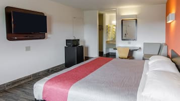 Habitación de hotel con cama, televisión, microondas, escritorio y baño visible a través de una puerta abierta.