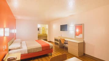 A hotel room with a bed, desk, chair, and a TV mounted on the wall.