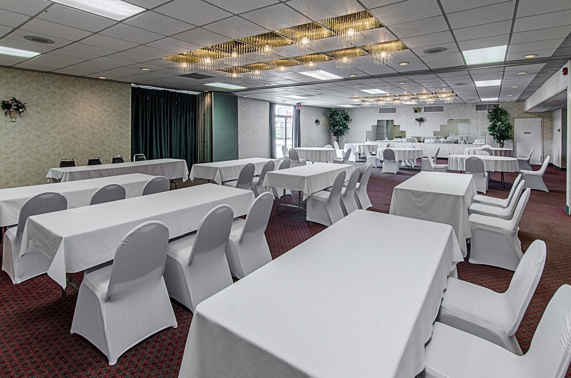A conference room with multiple tables and chairs, a patterned carpet, and a chandelier.