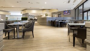 Un restaurant moderne au design épuré et à l’agencement ouvert, avec un plancher en bois, un mobilier contemporain et un grand écran de télévision fixé au mur.