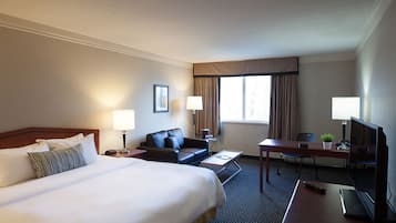 Quarto de hotel com uma cama grande, uma escrivaninha com um computador, uma televisão, um sofá e duas luminárias.