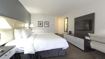 Una habitación de hotel con una cama grande, un escritorio con lámpara, un aparador, un espejo y un televisor instalado en la pared.