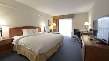 Una habitación de hotel con una cama grande, dos mesitas de noche con lámparas, un escritorio con una computadora y un televisor, y una silla.