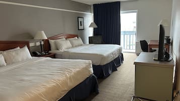 A hotel room with two beds, a desk with a computer, a chair, a lamp, and a view of the outdoors.